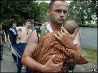 Sotilas kantaa vilttiin käärittyä vauvaa. Taustalla mies ilman paitaa.