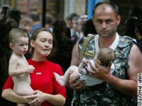 Punapaitainen nainen, alaston lapsi sylissään, seisoo vauvaa pitelevän sotilaan vieressä.