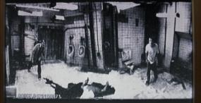 Valvontakamerakuva: kaksi miestä yleisessä WC:ssä, keskellä makaa ilmeisesti itsensä käsiaseella ampunut mies