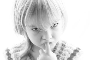 Mustavalkoinen kuva: vaaleatukkainen tyttö sormi suussa, ankarasti pinnistelevän näköisenä