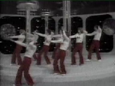 Punaisiin housuihin ja valkoisin D&A-paitoihin pukeutuneita ihmisiä jorailemassa 70-luvun tyyliin